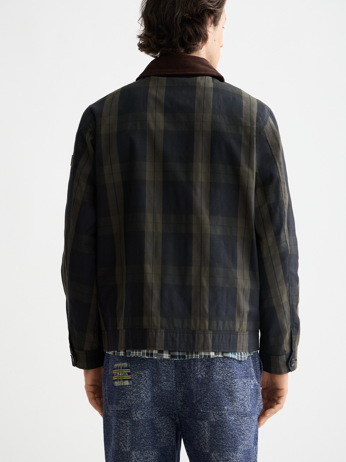 Scotch & Soda wax cotton jacket with front pockets and button closure, shown from the back in a natural outdoor setting.