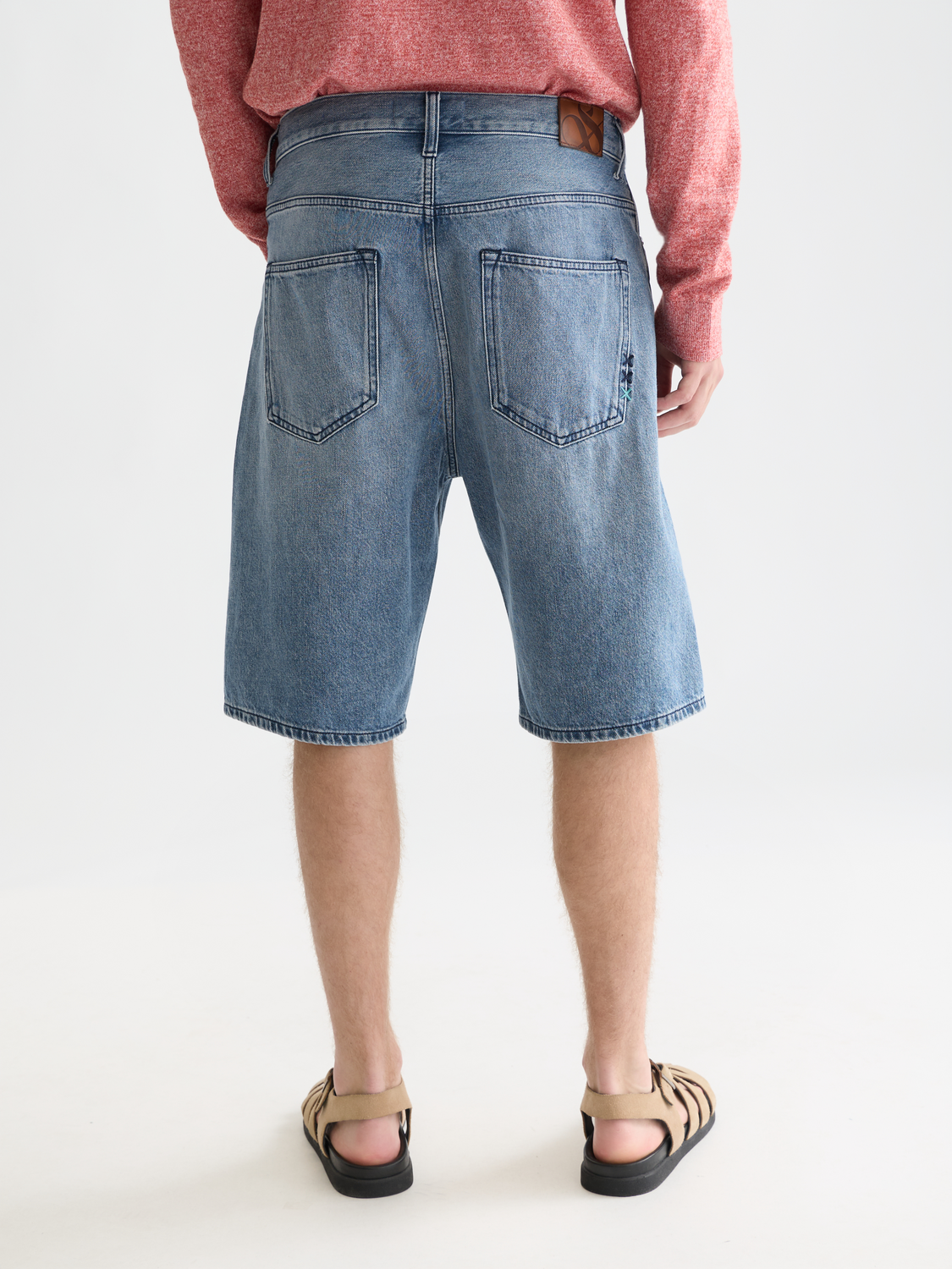 Back view of Scotch & Soda denim pitch loose-fit shorts with distressed details and rolled hems on model.