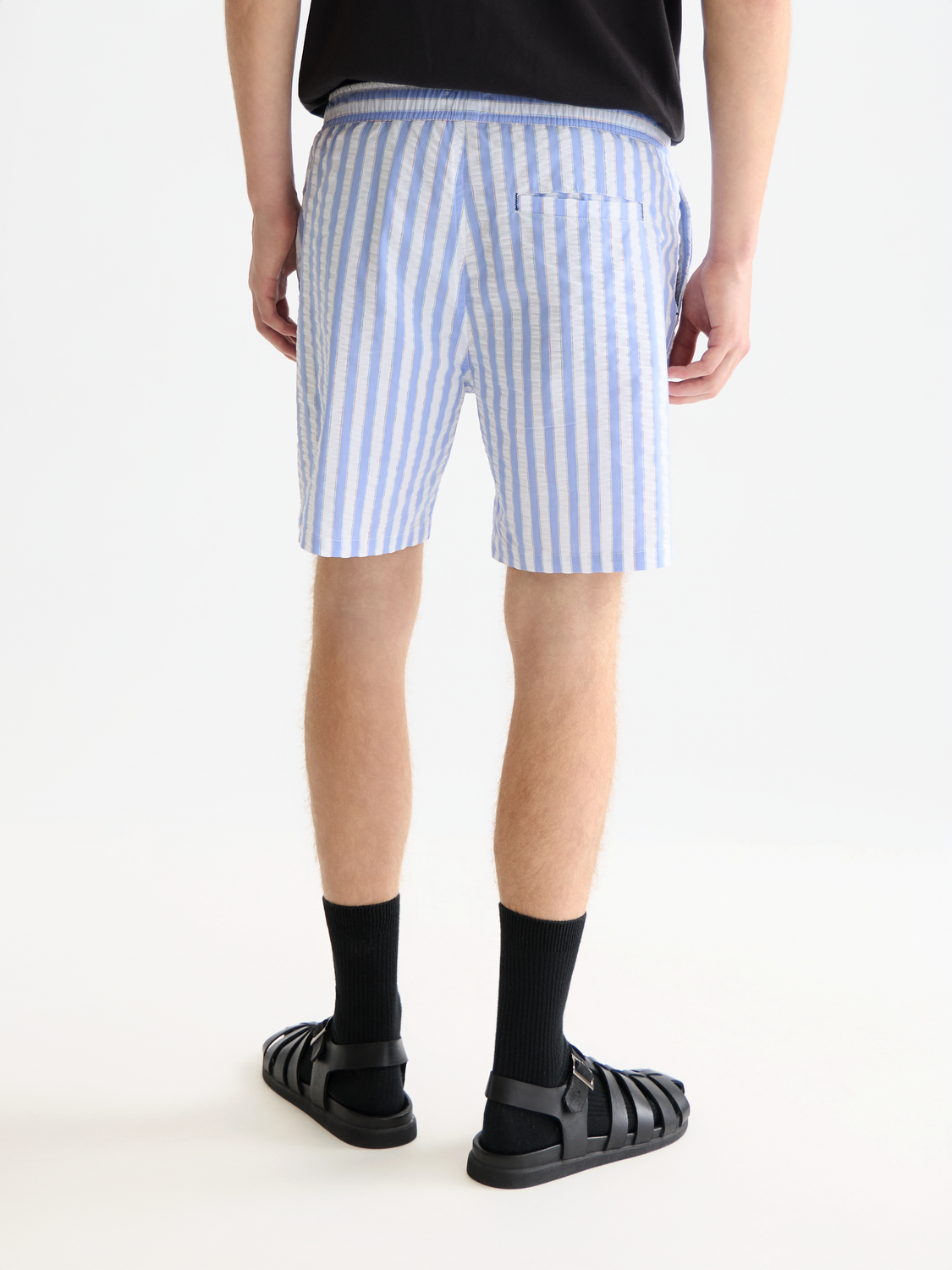 Striped mid-length swimshorts by Scotch & Soda with blue and white horizontal stripes, back view showing waistband and pocket.