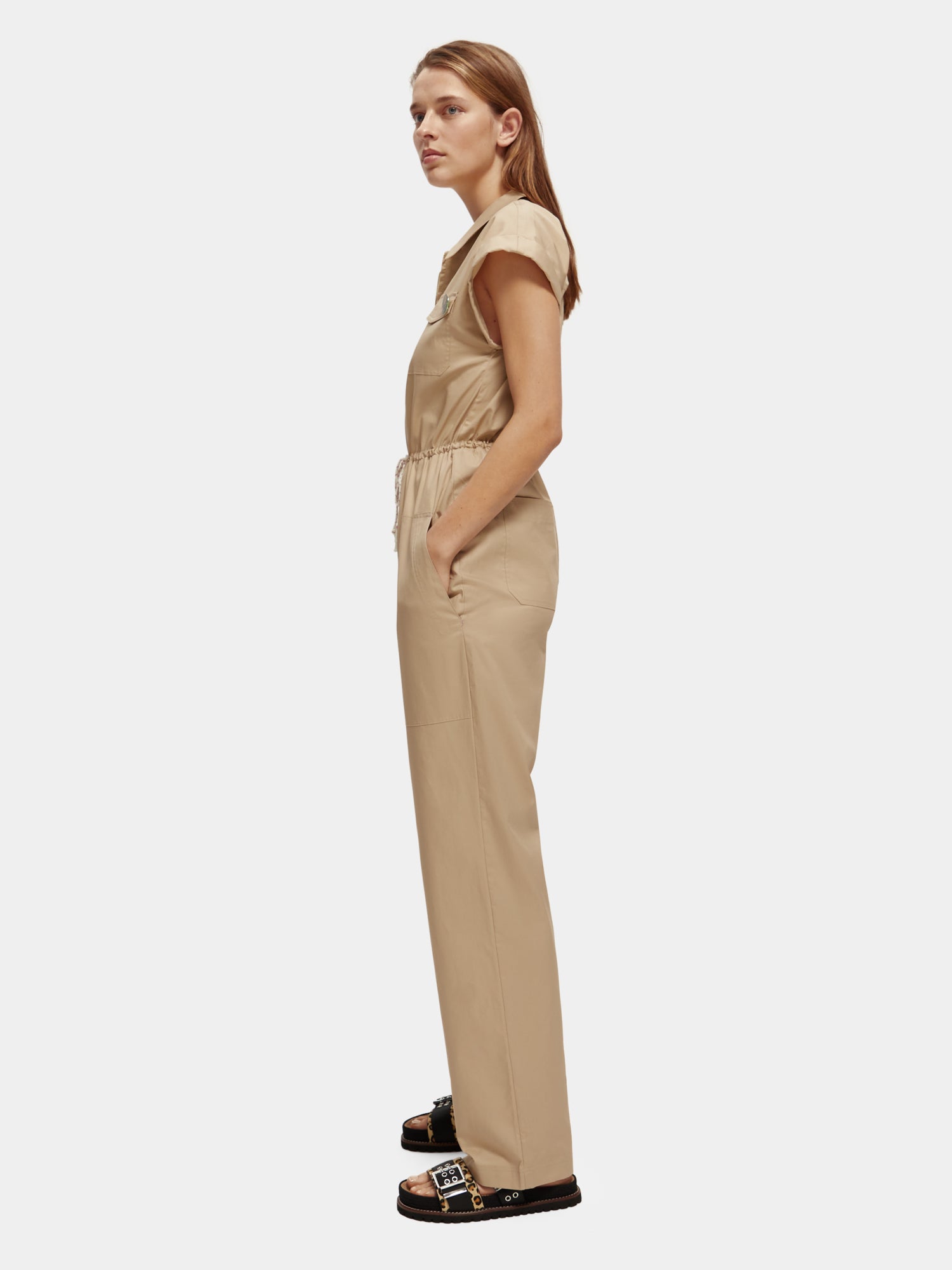 Military-style jumpsuit by Scotch & Soda, featuring functional pockets and a rugged design, displayed on a hanger.