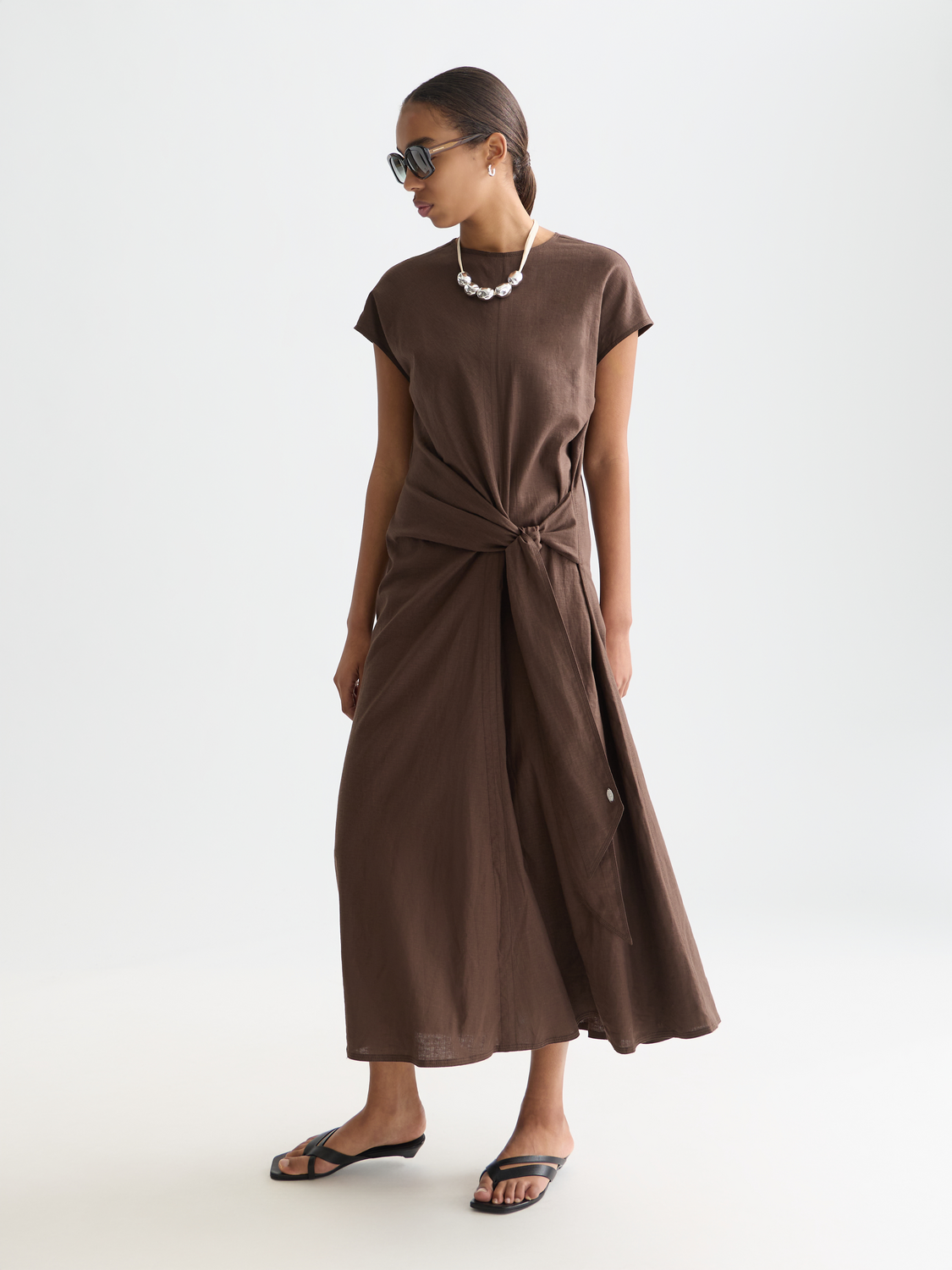Linen-blend tie dress by Scotch & Soda featuring a waist tie and relaxed fit, shown on a model in a casual outdoor setting.