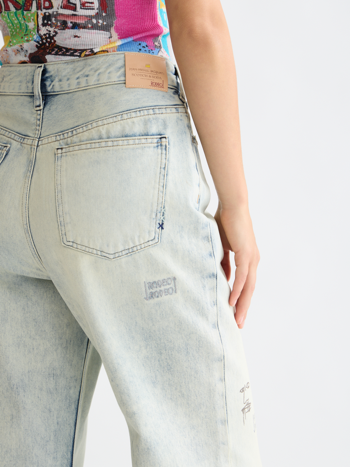 Pair of deep loose-fit denim jeans by SCOTCH & SODA featuring S&S x Basquiat collaboration logo and distressed details.