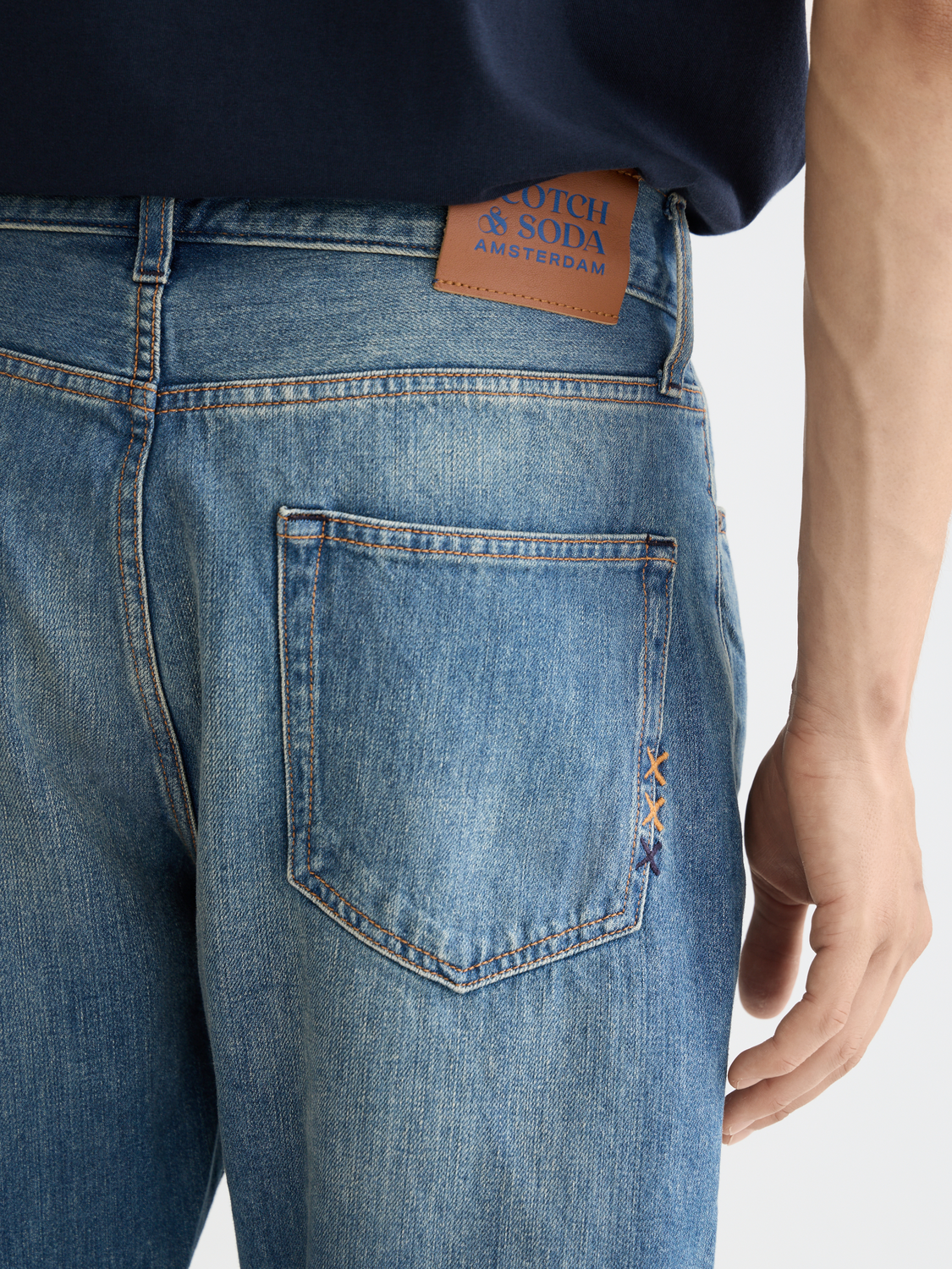SCOTCH & SODA Dean tapered denim jeans displayed on a hanger, showcasing their slim fit and classic blue denim fabric.