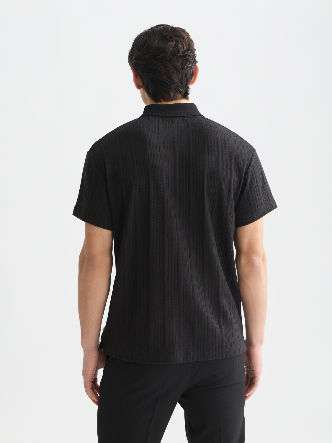 Black ribbed polo shirt by Scotch & Soda, displayed from the back with a classic collar and textured knit fabric.