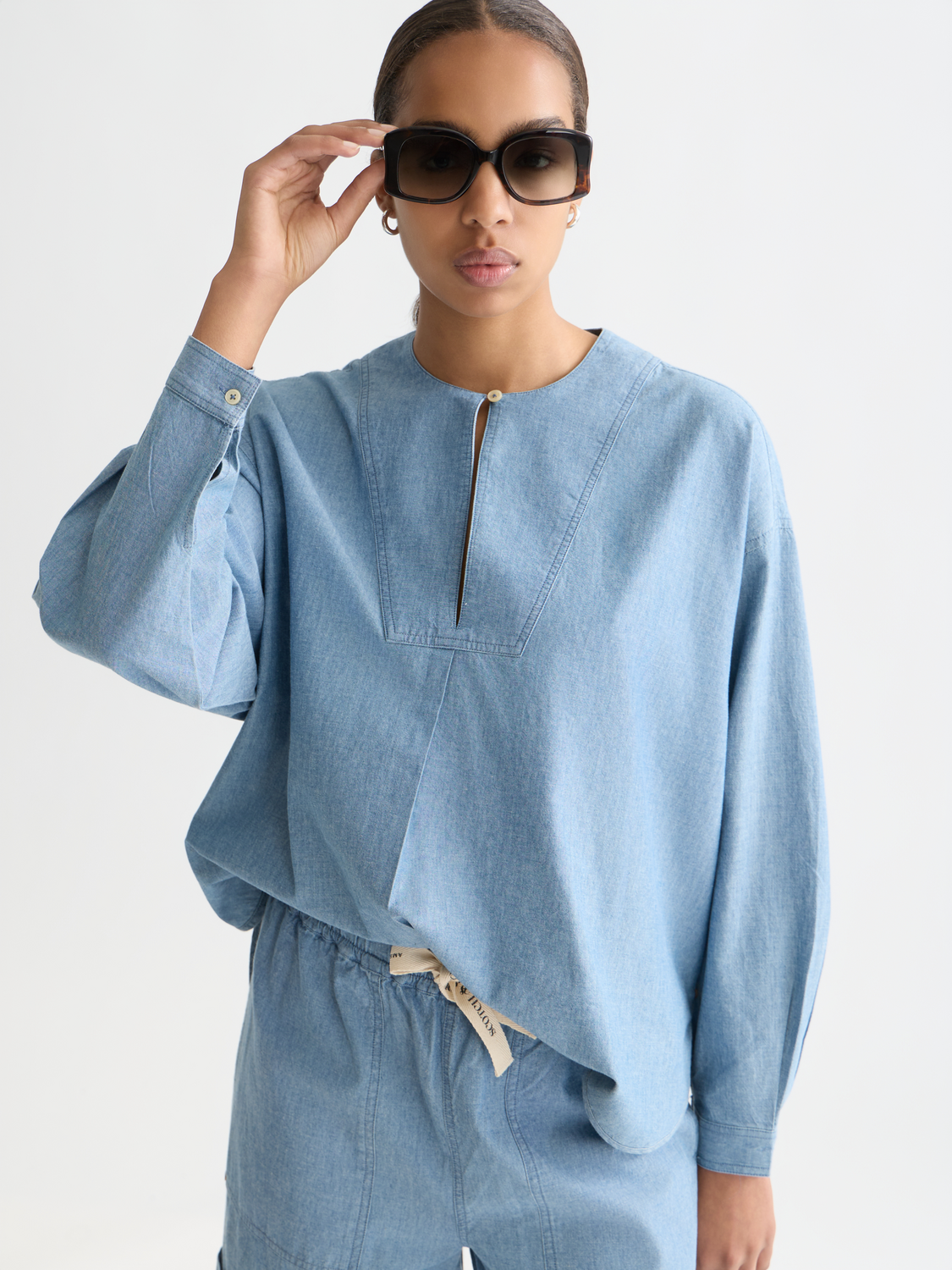 Scotch & Soda denim bib shirt woven top with adjustable straps and front pockets, displayed on a neutral background.