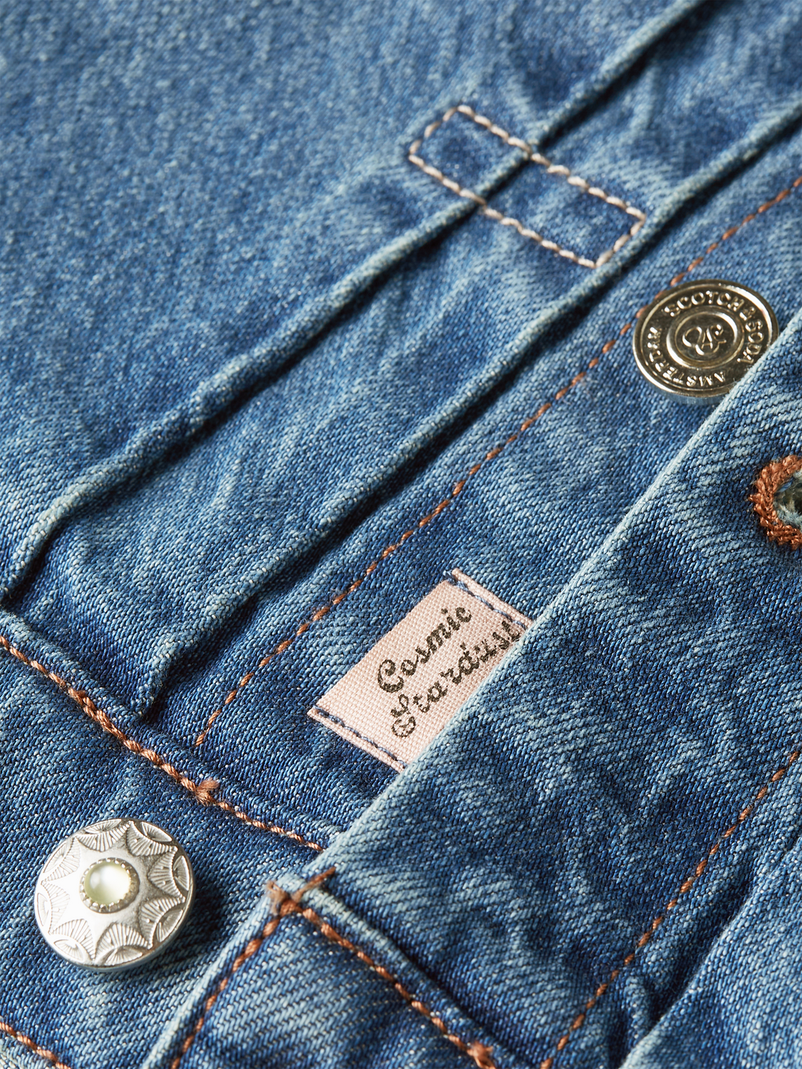 Scotch & Soda denim trucker jacket, classic blue jean style with button-up front and chest pockets, displayed on a hanger.