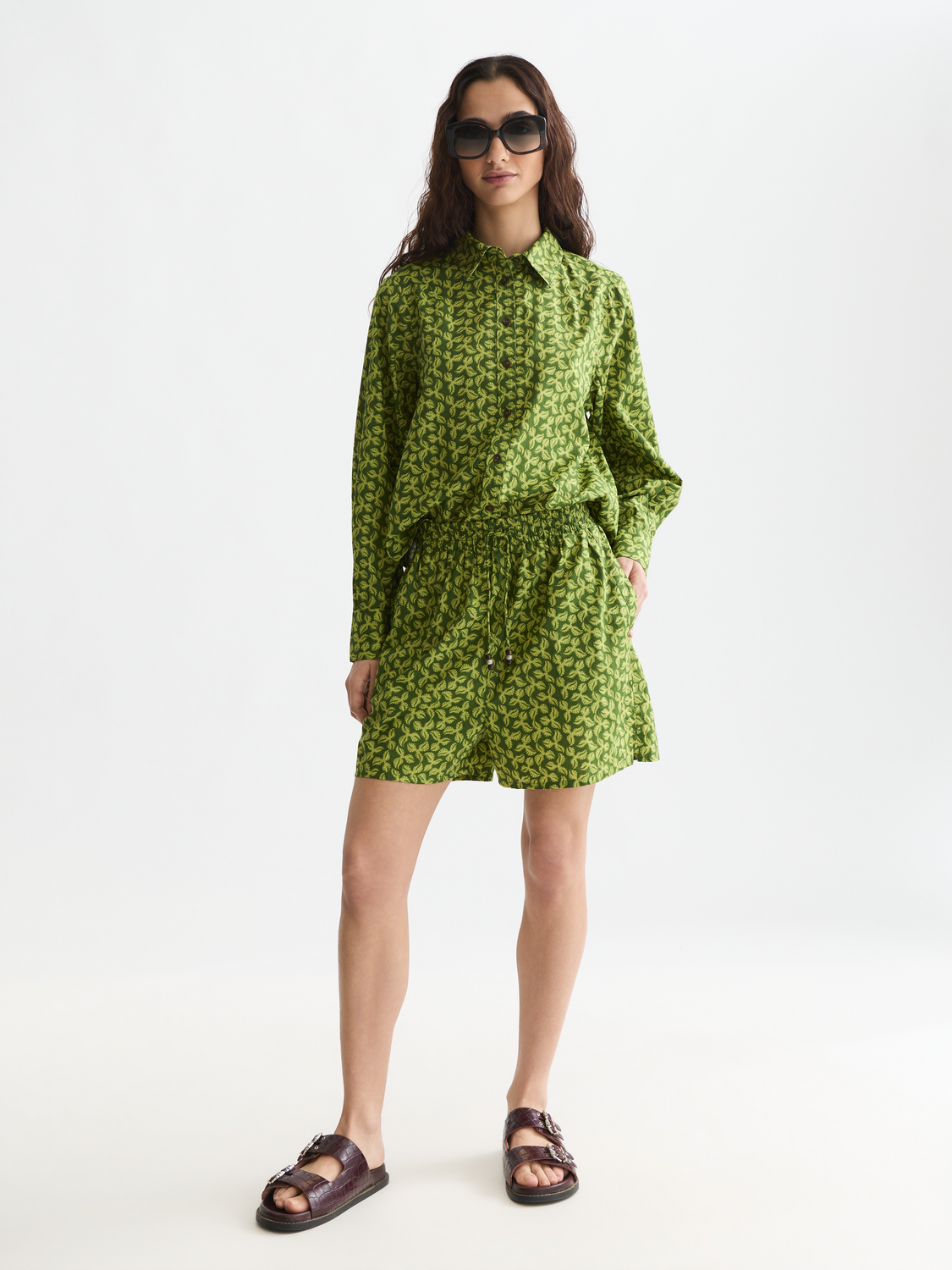 Printed shorts by Scotch & Soda featuring a colorful floral pattern, shown on a model with a casual outdoor setting.